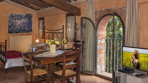 A dining area with a wooden table, chairs, a TV, and a view of greenery through a glass door. - Tenuta San Giovanni Alloro (lucca)