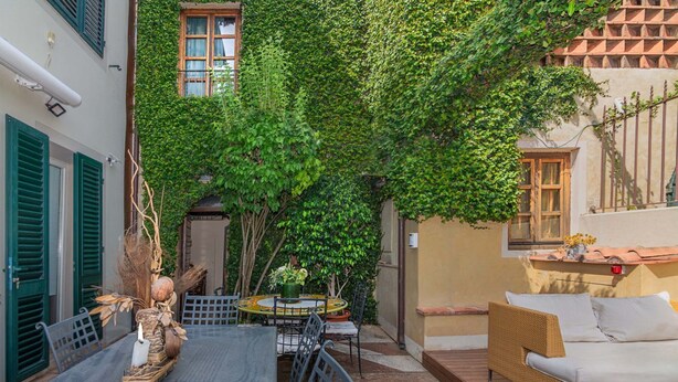 A courtyard with a dining table, chairs, a wicker sofa, and a potted plant. - Tenuta San Giovanni Alloro (lucca)