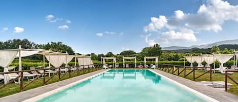 A rectangular pool with a wooden deck, surrounded by white canopies and lounge chairs.