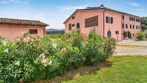 A pink building with a tiled roof, surrounded by green plants and flowers. - Tenuta San Giovanni Grapefruit (Lucca)