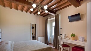 Un dormitorio con cama, escritorio con silla, televisor y ventana con cortinas.