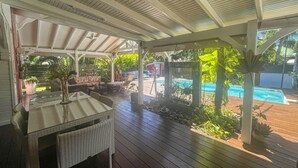 Un espacio al aire libre cubierto con piso de madera, mobiliario de mimbre y vista a una piscina.