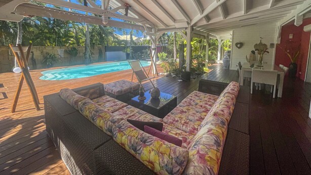 Un espacio al aire libre techado con piscina, mobiliario de descanso y una mesa de comedor.