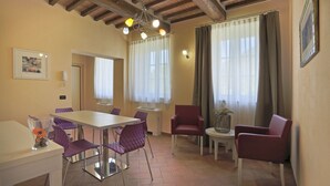 A dining area with a table and chairs, a ceiling with exposed beams, and a window with curtains. - Tenuta San Giovanni - Camomilla Apartment (Lucca)