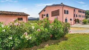 A pink building with a tiled roof, surrounded by green plants and flowers. - Tenuta San Giovanni - Camomilla Apartment (Lucca)