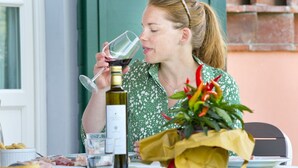 A person sitting at a table with a bottle of wine, a glass, and a bouquet of flowers. - Tenuta San Giovanni - Camomilla Apartment (Lucca)