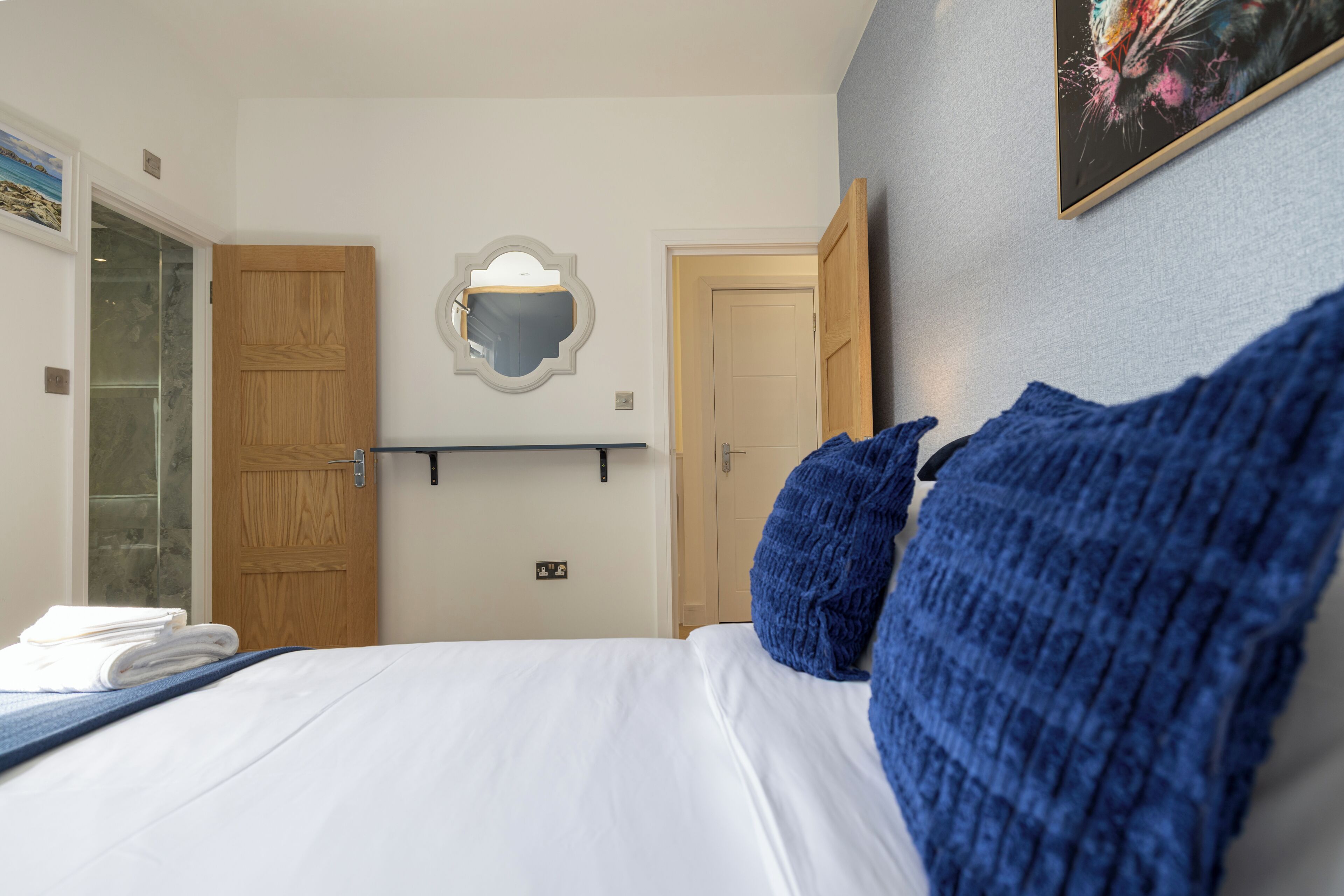 A hotel room with a bed, a wooden door, a mirror, and a framed picture on the wall.