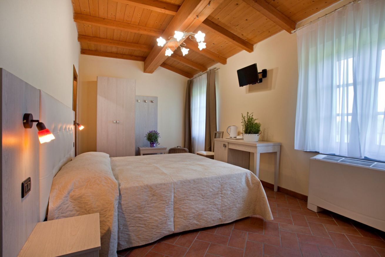 Een slaapkamer met een bed, een bureau, een stoel, een televisie en een raam met gordijnen.
