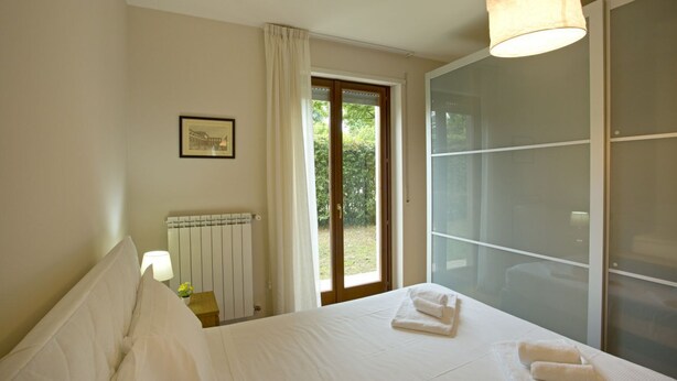 Una camera da letto con un letto, un termosifone, una finestra con tende e vista sul verde circostante.