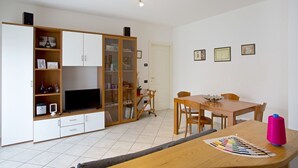 Un soggiorno moderno con televisore, mobili contenitori in legno, un tavolo da pranzo e una tabella colori.