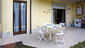 Un patio con tavolo apparecchiato per quattro, sedie bianche, una lavatrice e un’asciugatrice.