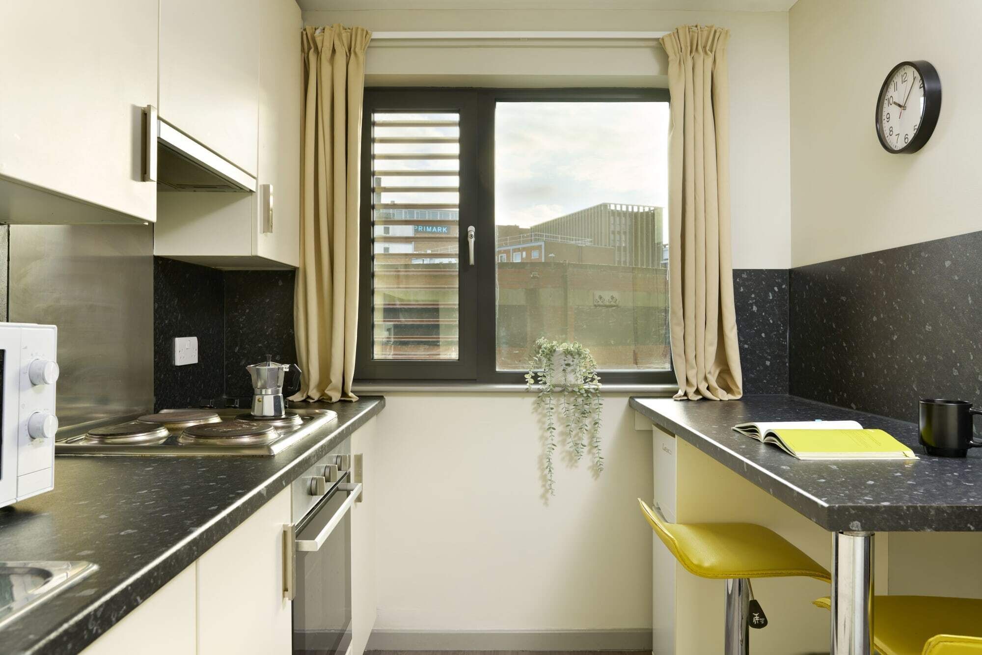 Une petite cuisine avec une fenêtre, une horloge et une chaise jaune.