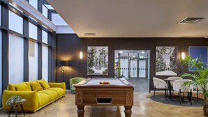 A pool table in a well-lit room with a yellow sofa and chairs, a small plant, and artwork on the walls. - For Students Only Ensuites in Coventry (Coventry)