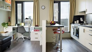 A modern kitchen with a dining area, a desk with a computer, and a small seating area with stools. - For Students Only Ensuites in Coventry (Coventry)