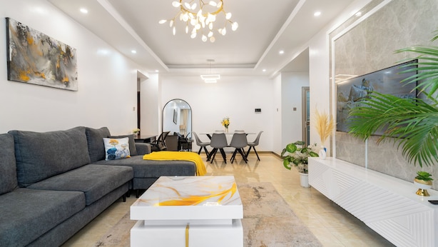Een moderne woonkamer met een bank, salontafel, eethoek en een televisie.