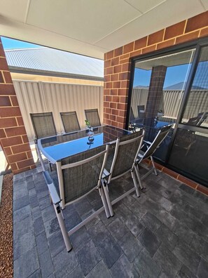 Een terras buiten met een glazen tafel en stoelen, bakstenen muren en uitzicht op de lucht.