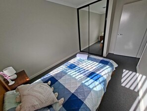 Een slaapkamer met een bed, nachtkastje, lamp en spiegel.