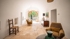 A spacious hallway with a stone floor, a wooden chair, a sofa, and a table with a green bowl. - Masseria il Pergolo (Martina Franca)