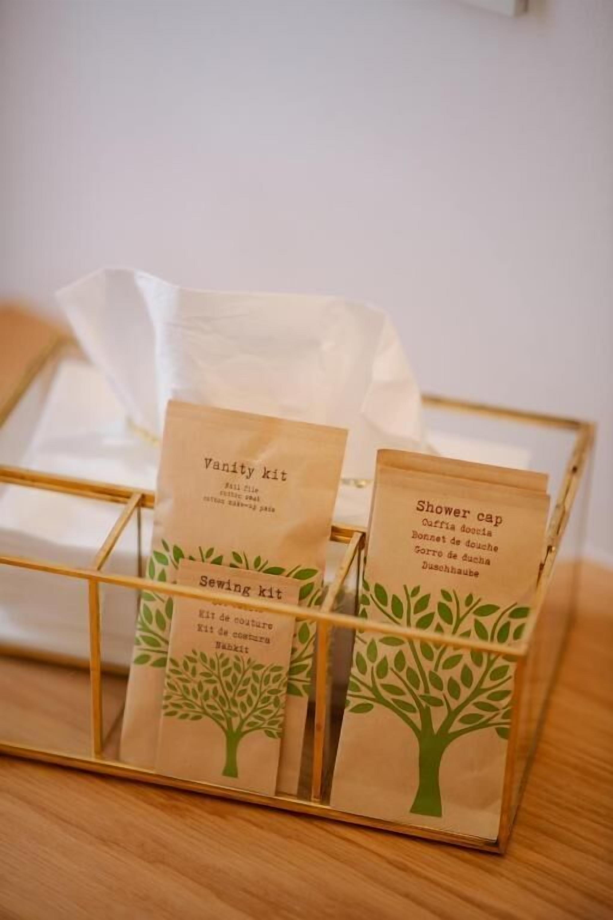 A wooden box with compartments containing labeled items: a vanity kit, a shower cap, and a sewing kit.