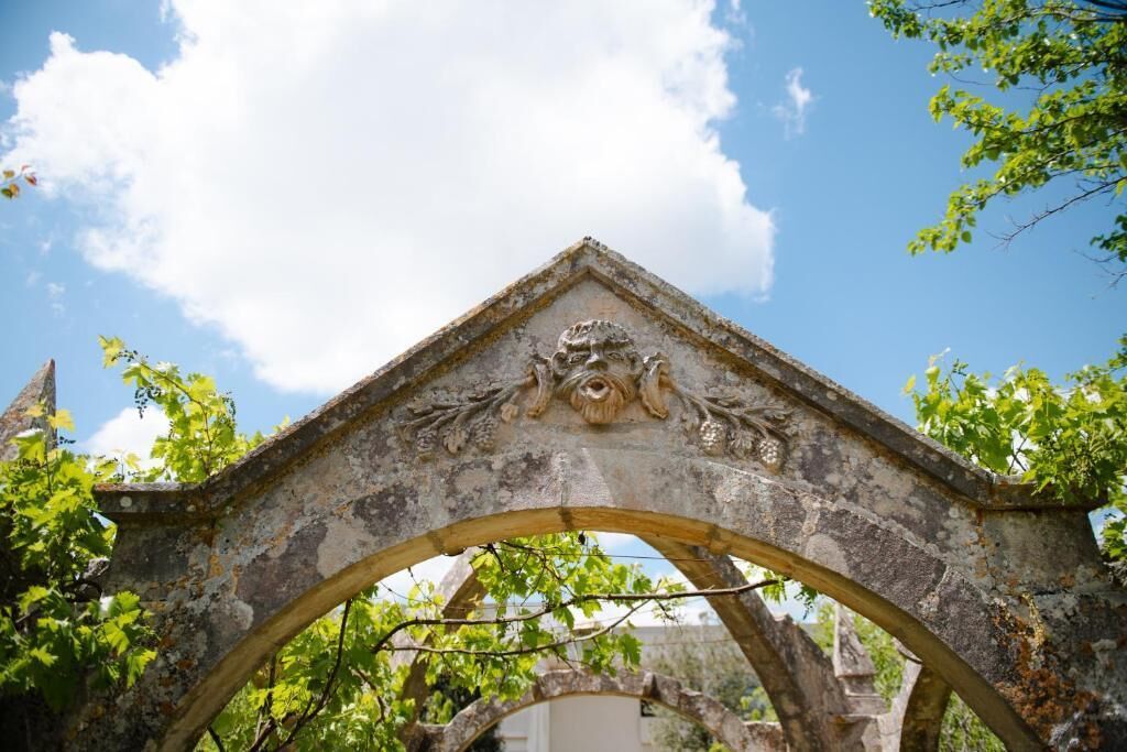 An old stone archway with intricate carvings, surrounded by greenery.