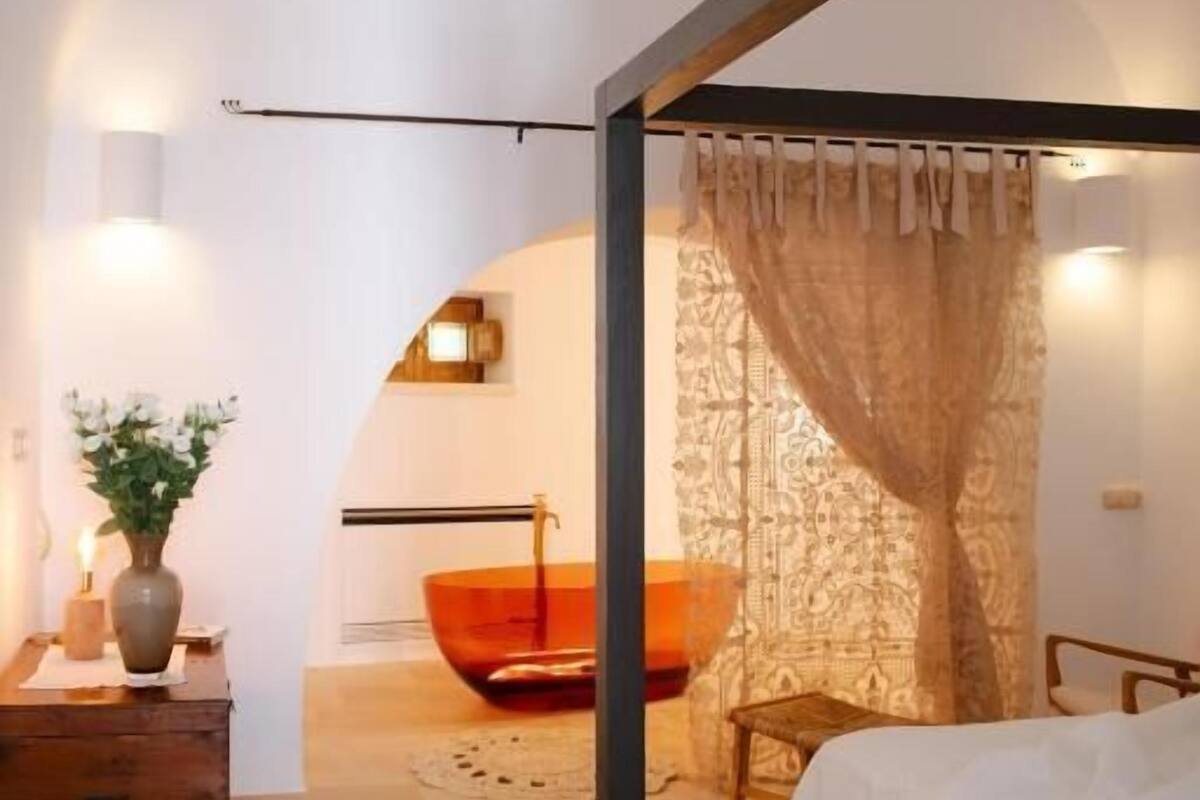 A modern bedroom with a bed, a nightstand, a vase with flowers, and a chair.