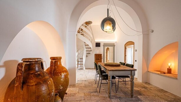 An interior with a dining area, stone flooring, and large vases. - Masseria il Pergolo (Martina Franca)