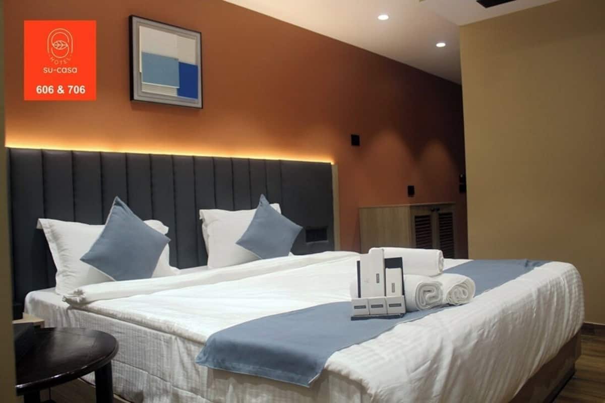 Una habitación de hotel con una cama grande, dos almohadas, una mesita de noche y un letrero en la pared con los números de la habitación.