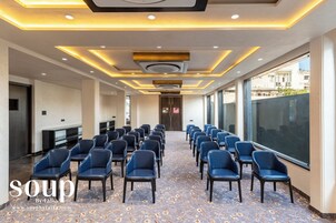 Un salón de conferencias con filas de sillas, alfombra estampada e iluminación de techo moderna.