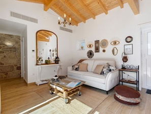 Een woonkamer met een witte bank, een glazen salontafel, een houten plafond en decoratieve wandversiering.