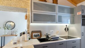 A modern kitchen with a stone wall, a clock, a sink, and a stove. - Vinha Da Touça T1 Holiday Home with Mountain View, Wi-Fi and Air Conditioning (Soajo)