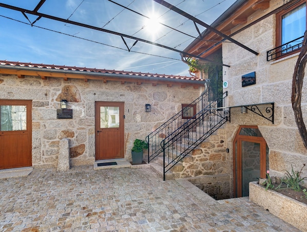 A stone building with a wooden door, a staircase with wrought iron railings, and a small garden area.