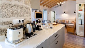 A kitchen with a stone wall, wooden ceiling, and a dining area with a sofa and table. - Vinha Da Touça T1 Holiday Home with Mountain View, Wi-Fi and Air Conditioning (Soajo)