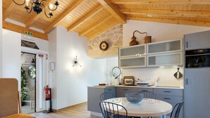 A modern kitchen with wooden beams, a dining table with chairs, and a built-in oven. - Vinha Da Touça T1 Holiday Home with Mountain View, Wi-Fi and Air Conditioning (Soajo)