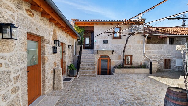 A stone building with a wooden door, a staircase leading to a second floor, and a cobblestone courtyard. - Vinha Da Touça T1 Holiday Home with Mountain View, Wi-Fi and Air Conditioning (Soajo)