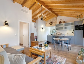 A cozy living room with a wooden ceiling, a dining area with a table and chairs, and a kitchen with modern appliances.
