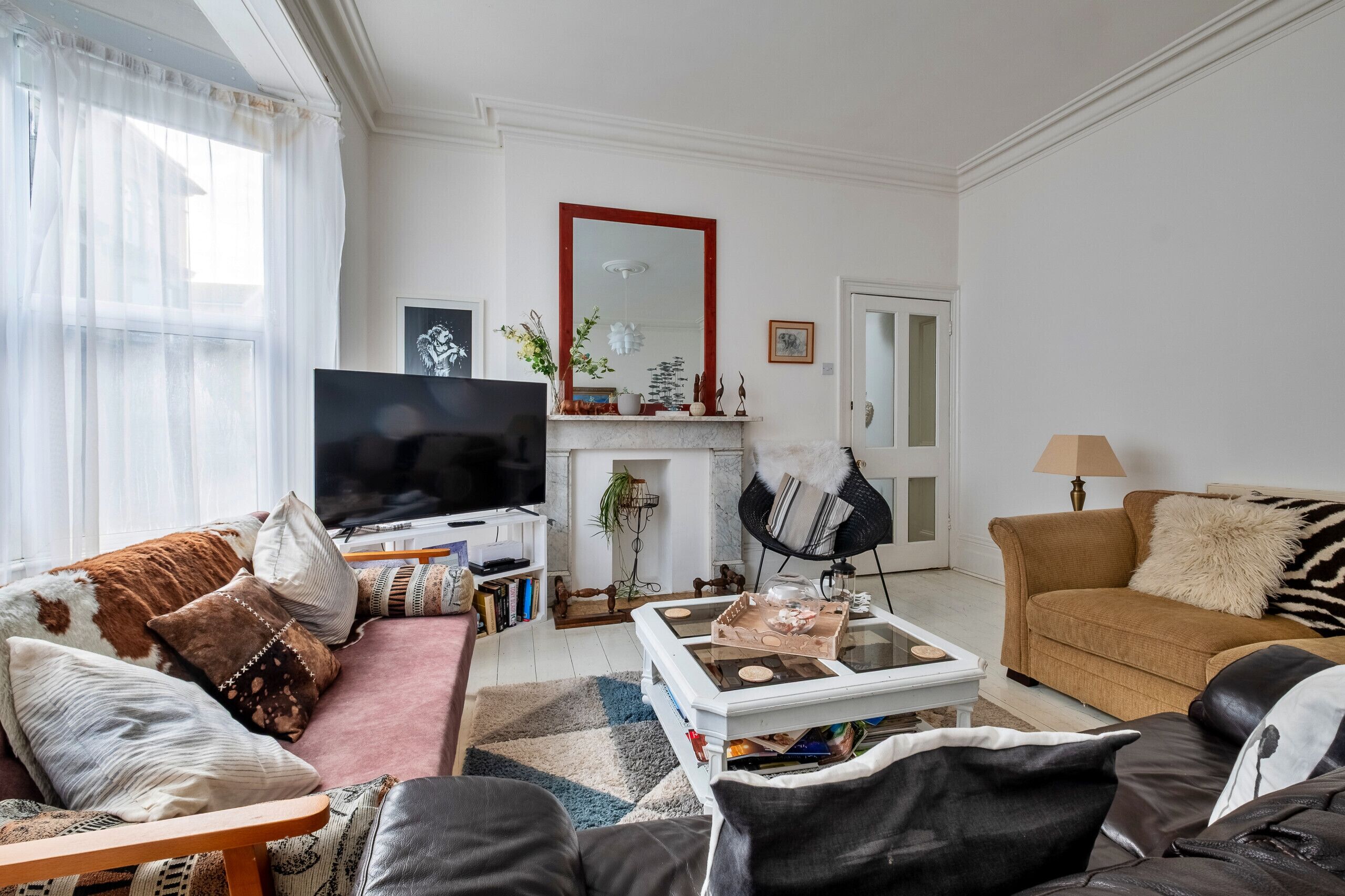 A living room with a sofa, armchairs, a coffee table, a TV, a fireplace, and a mirror.
