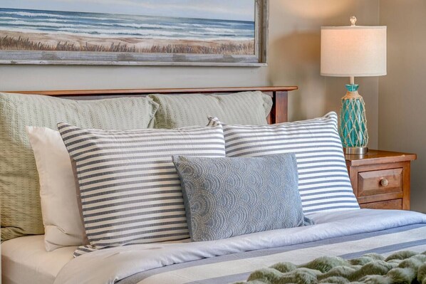 A bed with striped bedding, a decorative lamp, and a painting of a beach scene.