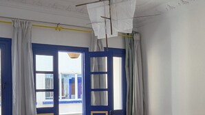 Une chambre à coucher comprenant un lit, une table de chevet, une commode, une fenêtre avec des rideaux et un ventilateur de plafond.