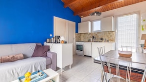 Una sala de estar con un sofá, una mesa de centro con un libro, una mesa de comedor con sillas, una cocina con armarios y una estufa, y una puerta con diseño.