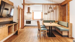 A modern kitchen with wooden cabinets, a built-in oven, and a dining area with a bench and table. - Regitnig‑Lake‑Hideaway am Weissensee (Weissensee)