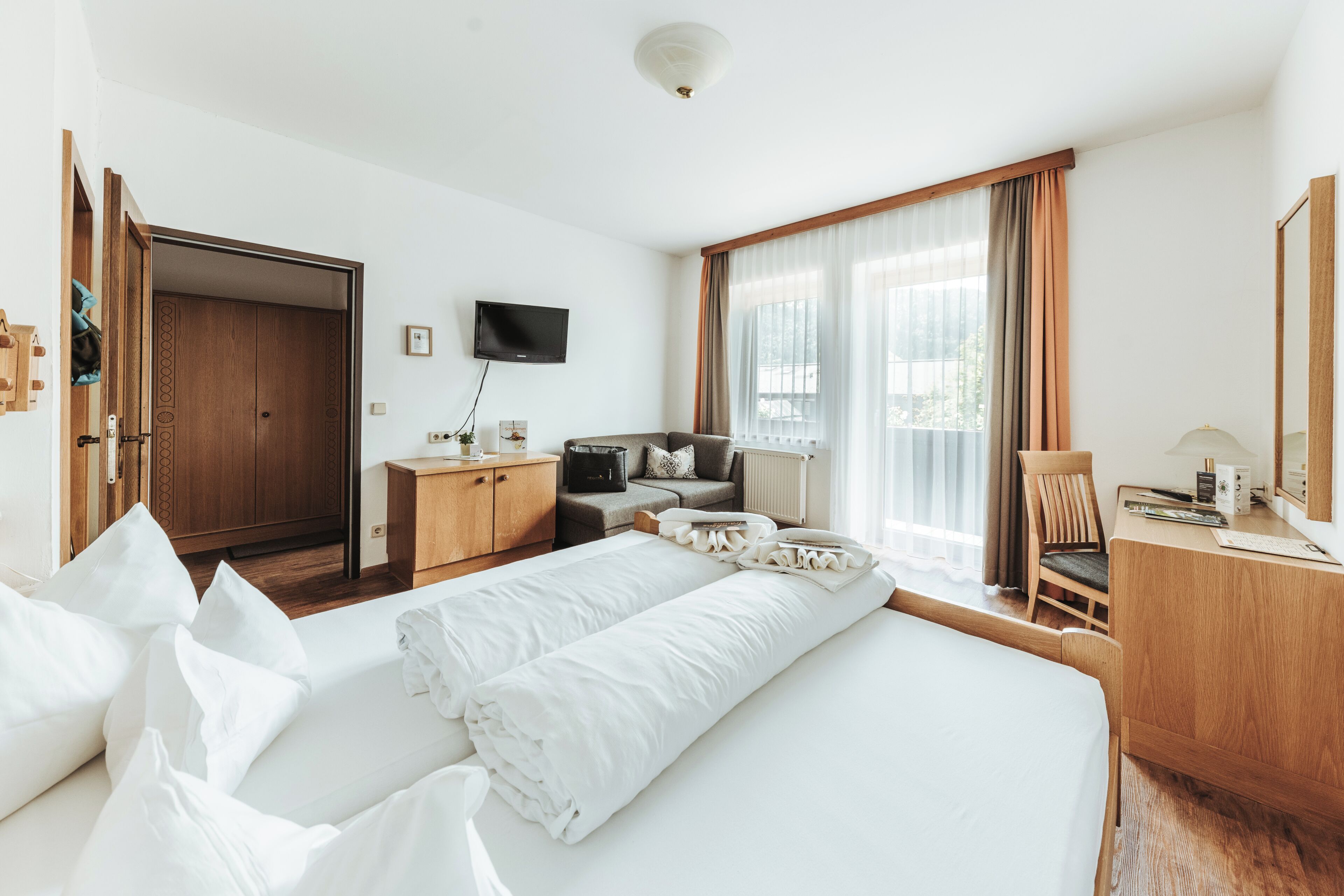 A hotel room with a bed, a desk, a chair, a television, and a wardrobe.