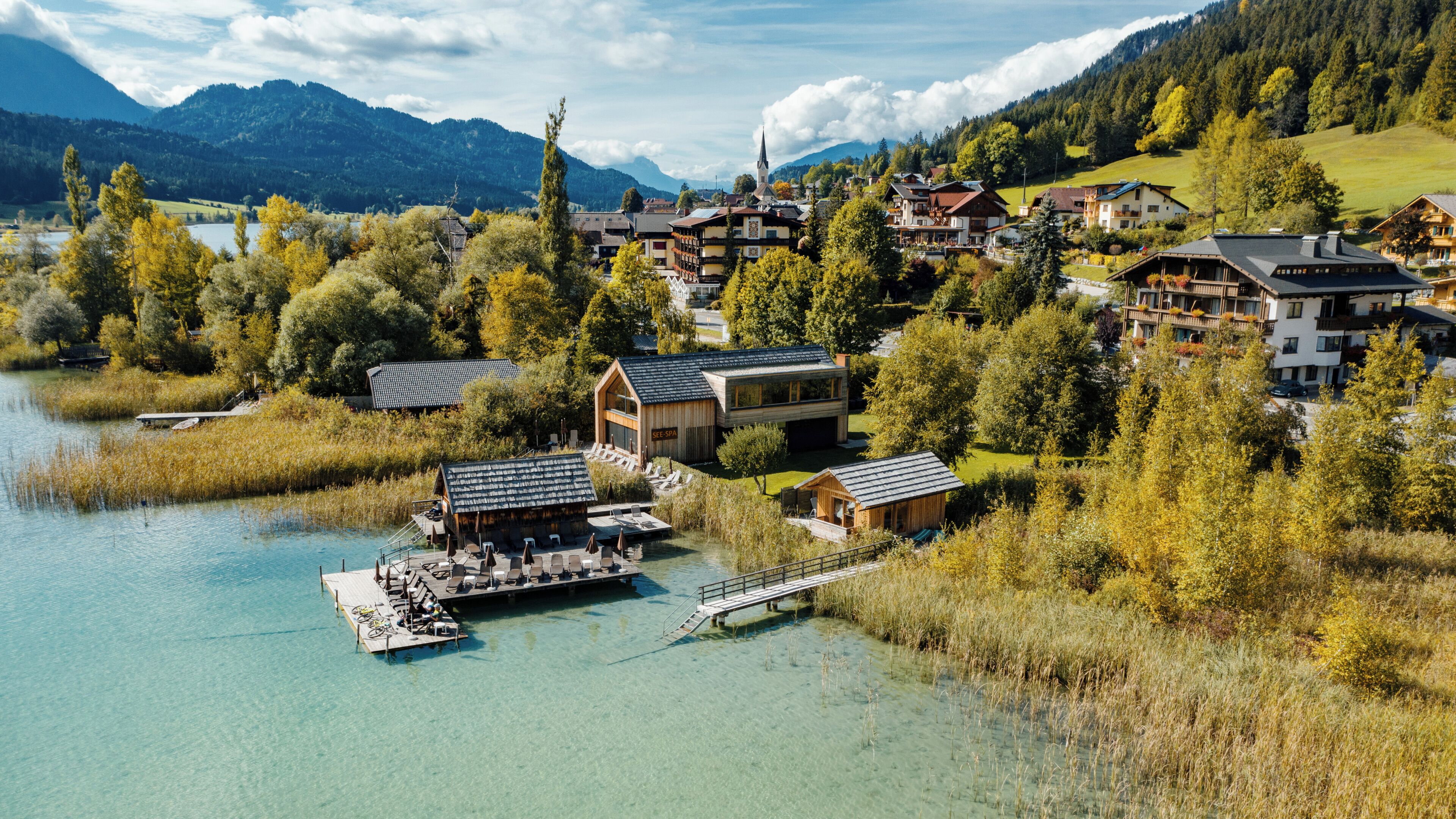 A lakeside resort with wooden cabins, a dock, and a mountain backdrop.