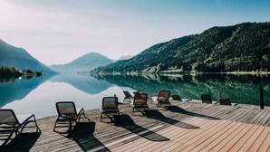 A wooden deck with lounge chairs overlooking a calm lake and forested mountains. - Regitnig‑Lake‑Hideaway am Weissensee (Weissensee)