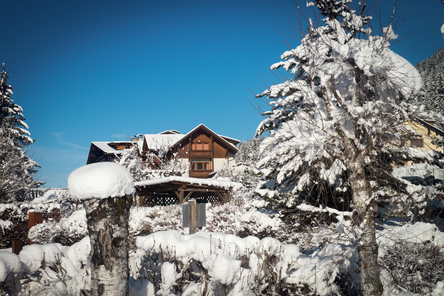 Una cabaña de madera con balcón, rodeada de árboles cubiertos de nieve y un cielo azul despejado.