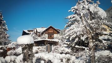 Una cabaña de madera con balcón, rodeada de árboles cubiertos de nieve y un cielo azul despejado.