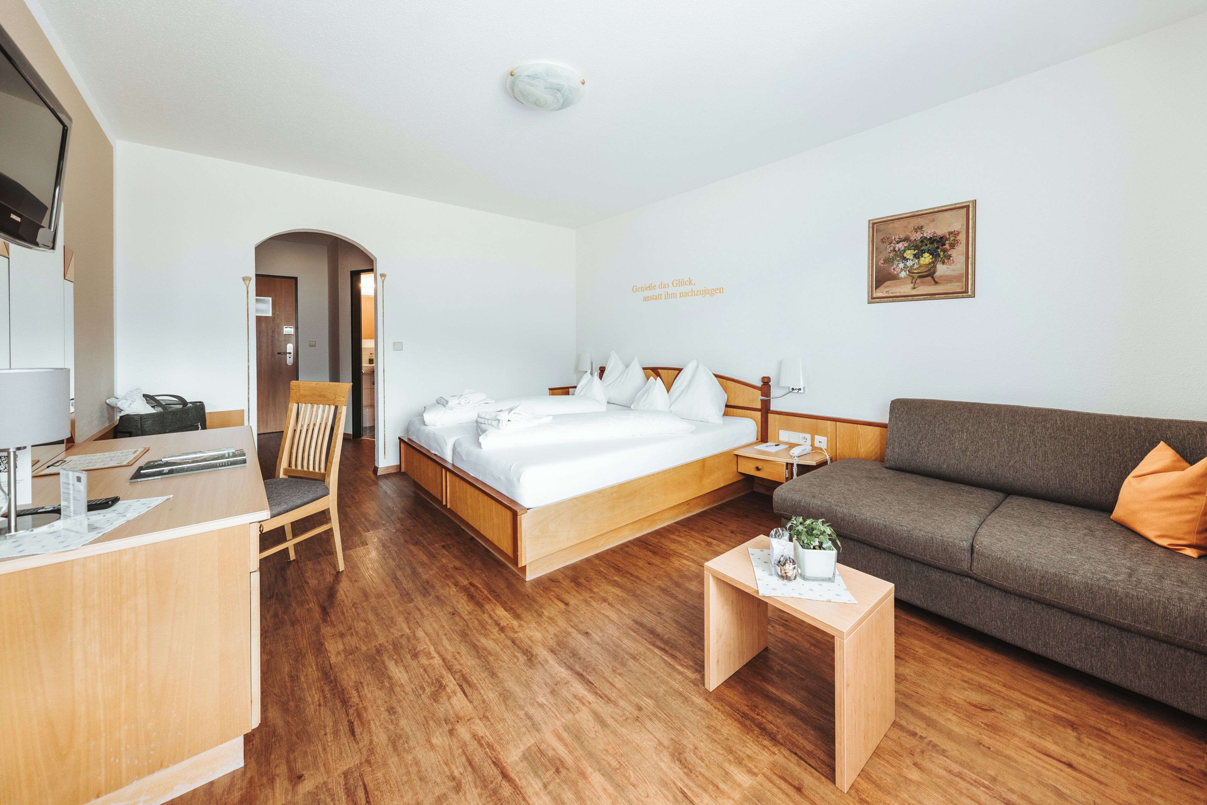 A hotel room with a bed, a sofa, a desk, and a small table with a plant.