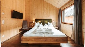 A wooden-paneled room with a bed, a flat-screen TV, and a window with curtains. - Regitnig‑Lake‑Hideaway am Weissensee (Weissensee)