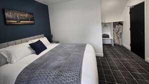 A modern hotel room with a large bed, a painting on the wall, a wardrobe, and a bathroom with a black door. - Woodside House (Forres)