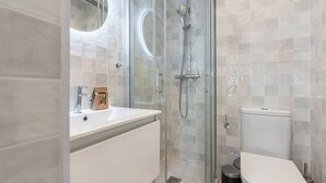Ein modernes Badezimmer mit einer gläsernen Dusche, einem weißen Waschbecken und einer Toilette.