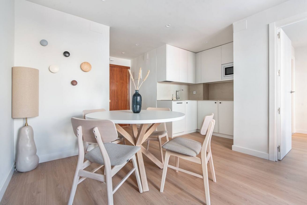 Una cocina moderna con armarios blancos, un microondas y un comedor con una mesa redonda y cuatro sillas.